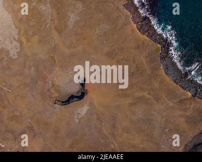 Landschaft auf der Halbinsel Reykjanes in Island. Tagesansicht von oben auf einen erloschenen Vulkankrater. Schatten auf altem Krater-Rand in brauner Sandoberfläche. Stockfoto