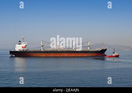 Piräus, Athen, Griechenland - 2022. Juni: Das große Frachtschiff Stella GS wird mit einem Schlepper in den Hafen von Piräus geführt. Stockfoto