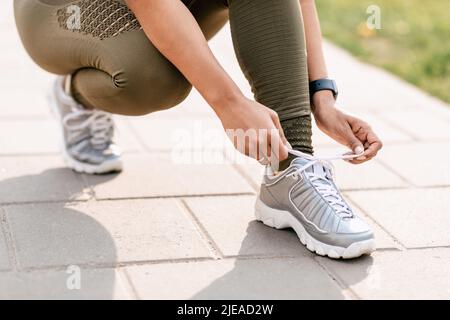 Die schwarze Millenial-Sportlerin schnürt ihre Schuhe, während sie im Park joggt, aus der Nähe der Beine Stockfoto