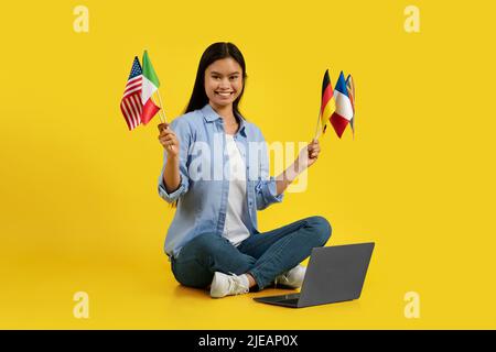Frohes tausendjähriges koreanisches Lehrerin mit vielen verschiedenen Flaggen, die auf dem Boden mit einem Laptop sitzen Stockfoto