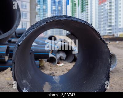 Riesige schwarze Pfeife im Vordergrund und verschwommene Baustelle mit Hochhäusern im Hintergrund in Kiew, Ukraine. Neuer Bezirk im Bau. Stockfoto