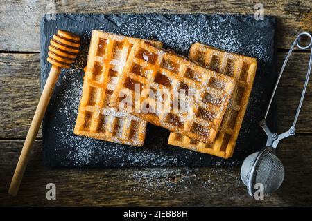 Süße Waffeln, mit Honig beträufelt und mit Puderzucker auf einem Schiefer bestreut Stockfoto
