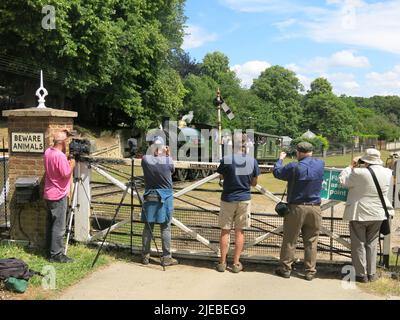 Kameras bereit wartet eine Reihe von Männern an der Kreuzung, um den herannahenden Dampfzug zu fotografieren, der entlang der historischen Eisenbahnlinie kommt. Stockfoto