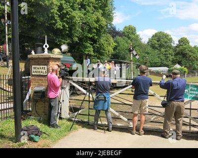 Kameras bereit wartet eine Reihe von Männern an der Kreuzung, um den herannahenden Dampfzug zu fotografieren, der entlang der historischen Eisenbahnlinie kommt. Stockfoto