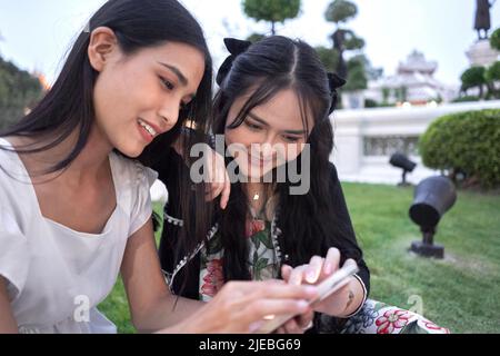Zwei lächelnde Freunde, die das Handy gemeinsam in einem Garten eines buddhistischen Tempels benutzen Stockfoto