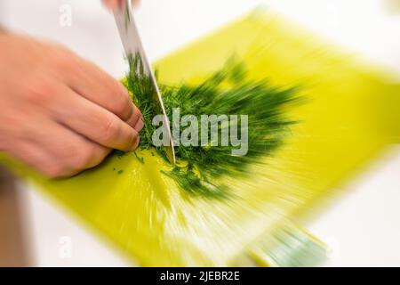 Draufsicht auf den Mann, der Dill zum Salatmachen mit Küchenmesser schneidet, Bewegungsunschärfe-Effekt Stockfoto