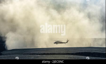Silhouette eines militärischen Black Hawk-Hubschraubers, der in einer Staubwolke landet oder abfliegt Stockfoto