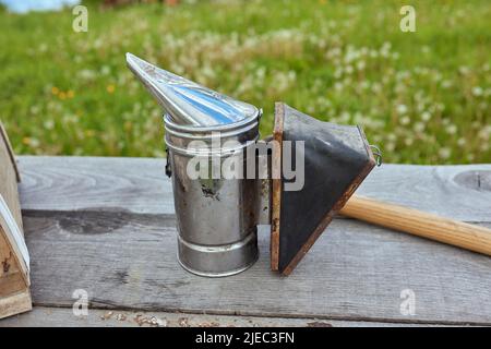 Bienenraucher auf der Oberseite eines Bienenstocks an einem Sommermorgen rauchen. Eine Grundausstattung der Imkerei. Bienenzuchtkonzept Stockfoto