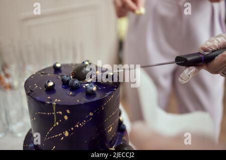 Schwarzer Stockkuchen auf dem dunkelschwarzen Hintergrund mit goldenen Sternen und Kugeln Dekoration auf der Oberseite. Luxuriöse Geburtstagstorte Stockfoto