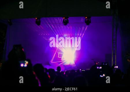 Violette Laser-Neonstrahlen. Menschenmenge, die beim Straßenfest eine Lasershow ansieht. Viele Menschen genießen das Konzert. Stockfoto