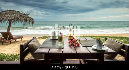 Restaurant oder Cafe am Strand. Tischkulisse mit Cocktail und Blumen auf Meeresgrund in tropischem Resort. Panoramablick auf das wunderschöne romantische Abendessen Stockfoto