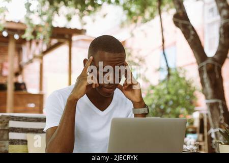 Erschöpfter, gestresster, multirassischer Mann mit dunkler Haut in einer Brille, der die Hände am Kopf hielt, litt und die Augen vermasselte Stockfoto