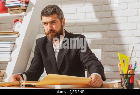 Porträt eines ernsthaften Lehrers im Klassenzimmer. Tutor, Professor, Mentor Mann am Schreibtisch. Studium, Lernen, Trainingskonzept. Stockfoto