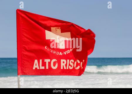 Rote Stromsignalflagge, geschrieben hohes Risiko an einem Strand in Rio de Janeiro. Stockfoto