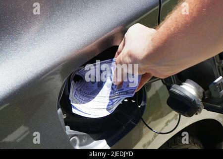 Die Hand des Mannes schiebt Geld in den Tank des Autos. Konzept der hohen Kraftstoffpreise, Kraftstoffkrise Stockfoto