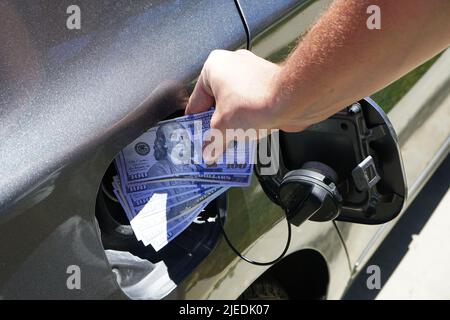 Die Hand des Mannes ist dabei, die Währung in den Tank des Autos zu schieben. Konzept der hohen Kraftstoffpreise, Kraftstoffkrise Stockfoto