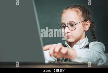 Schüler arbeiten auf Laptop-Computer über Tafel Hintergrund. Kind in der Nähe der Tafel in der Schule Klassenzimmer. Kind lernt in der Klasse auf Hintergrund Stockfoto