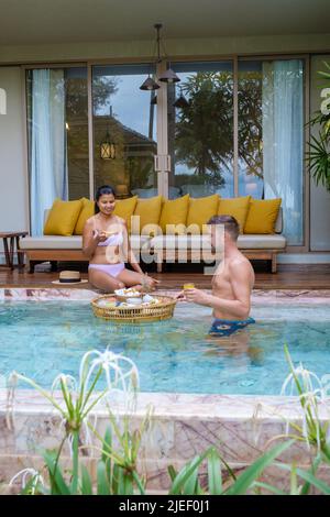 Ein paar Männer und Frauen beim Frühstück im Pool in einer Pool-Villa während des Urlaubs. Paar auf einem Luxusurlaub in Thailand, schwimmende Frühstück Stockfoto