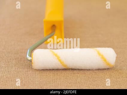 Nahaufnahme einer Walze mit einem gelben Griff und einem rustikalen Stoffhintergrund. Stockfoto