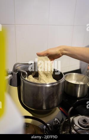 Der Prozess der Herstellung von Weizenbrot in einer handwerklichen Bäckerei. Knetmasse in einem Teigmischer kneten. Vertikales Foto. Stockfoto