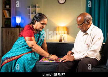 Ältere Paare spielen Schlangenleiter Spiel, während sie auf dem Sofa zu Hause sitzen - Konzept der Unterhaltung, Ruhestand Freizeitaktivitäten und Bindung Stockfoto