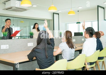 Büroschulung läuft, wobei die Auszubildenden die Hände heben, um Fragen zu stellen. Co Working Office-Einstellung. Stockfoto