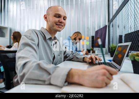 Junger kahler Geschäftsmann, der im Büro am Schreibtisch sitzt und am Computer arbeitet Stockfoto