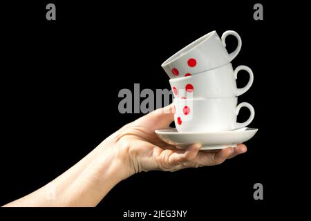 Kaffeetassen in roten Punkten stapeln sich in der Hand isoliert auf schwarzem Hintergrund. Stockfoto