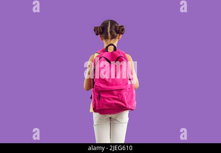 Neue geräumige rosa Schulrucksack auf der Rückseite des kleinen Mädchens, isoliert auf lila Hintergrund. Stockfoto