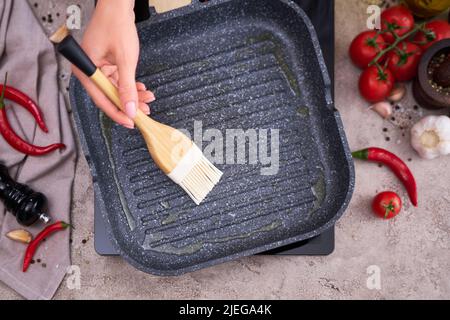 Frau schmieren Olivenöl auf der Grillpfanne mit Silikonbürste in der heimischen Küche Stockfoto