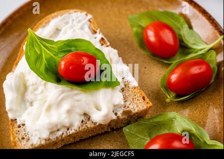 Brot mit Mozarella-Käse, Kirschtomate auf Basilikumblättern auf braunem Teller, Nahaufnahme. Stockfoto