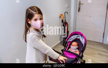 Mädchen mit Gesichtsmaske bereit für einen Spaziergang zu gehen Mit ihrer Puppe mit Maske Stockfoto