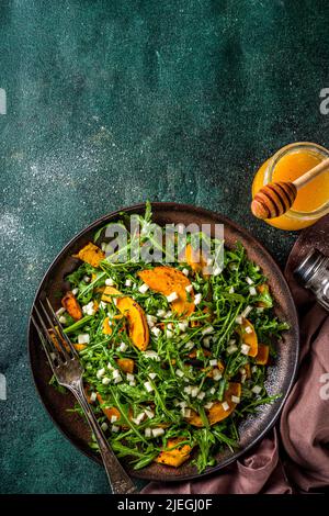 Hausgemachter Kürbissalat mit gegrillten Kürbisscheiben, Rucola und Käse. Herbst Kürbis Salat Rezept, dunklen Hintergrund kopieren Raum Stockfoto