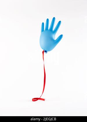 Blauer, aufgeblähter Medizinhandschuh mit rotem Band auf weißem Hintergrund. National Doctors Day Konzept. Stockfoto