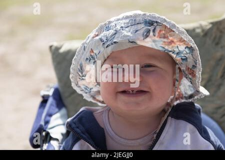 Umea, Norrland Schweden - 21. Mai 2022: Lachendes Baby mit neuen Zähnen und Sonnenhut Stockfoto