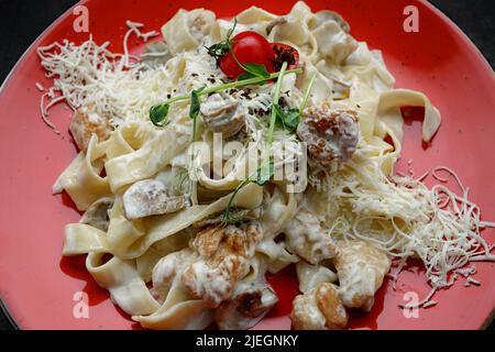 Fettuccine mit Huhn und Pilzen, auf einem Teller, auf dunklem Grund Stockfoto