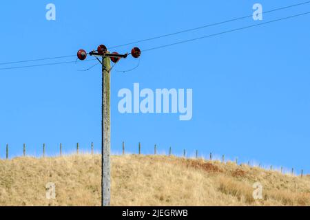 Stromkabel, die an einer Holzpoll mit einem blauen Himmel Hintergrund befestigt sind Stockfoto