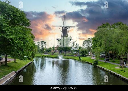 Niederländische Windmühle. Molen De Valk ist eine Turmmühle und ein Museum in Leiden, Holland. Reflexionen auf Kanalwasser, blauer wolkig Himmel bei Sonnenuntergang Stockfoto