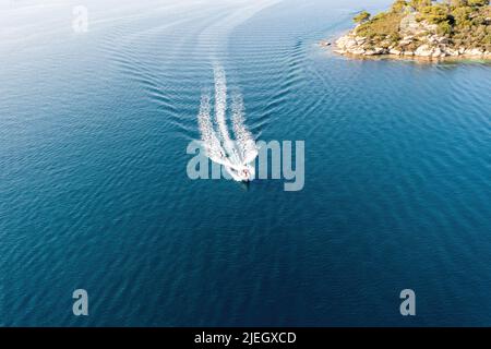 Motorboot, Schnellboot auf dem Hintergrund des wellig gekräuselten Meeres, weiße Wake. Urlaub Aegean Sea Griechenland im Sommer. Luftdrohnenansicht Stockfoto