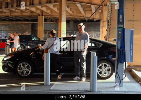 Leute, die ein seltenes Plug-NYC-Ladegerät für Elektrofahrzeuge am Straßenrand benutzen, um ihr Elektroauto in New York City aufzuladen. Das öffentliche EV-Netz ist .. (Siehe Info) Stockfoto