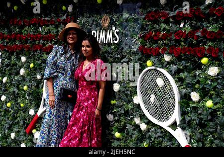 Am ersten Tag der Wimbledon Championships 2022 im All England Lawn Tennis and Croquet Club, Wimbledon, posieren die Zuschauer vor der Pimms-Blumenwand für Fotos. Bilddatum: Montag, 27. Juni 2022. Stockfoto