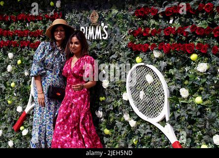 Am ersten Tag der Wimbledon Championships 2022 im All England Lawn Tennis and Croquet Club, Wimbledon, posieren die Zuschauer vor der Pimms-Blumenwand für Fotos. Bilddatum: Montag, 27. Juni 2022. Stockfoto