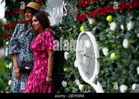 Am ersten Tag der Wimbledon Championships 2022 im All England Lawn Tennis and Croquet Club, Wimbledon, posieren die Zuschauer vor der Pimms-Blumenwand für Fotos. Bilddatum: Montag, 27. Juni 2022. Stockfoto