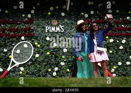 Am ersten Tag der Wimbledon Championships 2022 im All England Lawn Tennis and Croquet Club, Wimbledon, posieren die Zuschauer vor der Pimms-Blumenwand für Fotos. Bilddatum: Montag, 27. Juni 2022. Stockfoto