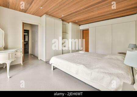 Komfortables Bett mit warmer Decke in der Nähe von Fenster und Tür, die zur Terrasse führt, in einem stilvollen Schlafzimmer mit grauen Wänden Stockfoto