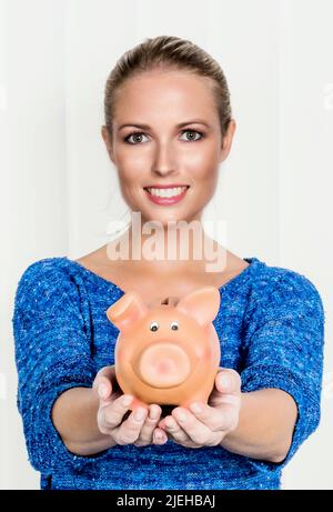 Eine junge Frau hält ein Sparschwein in ihrer Hand. Symbolfoto für Spare, Geld anlegen und Altersvorsorge. Stockfoto