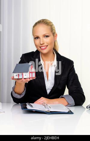 Eine junge Immobilien Maklerin mit einem Modellhaus in seinem Büro. 30,35, Jahre, Blonde, Frau, Sommersprossen, Stockfoto