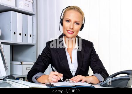 Eine freundliche junge Frau mit Headset im Kundendienstcenter telefoniert mit einem Kunden. Freundliche Hotline, Mitarbeiterin, Call Center, Sekretäre Stockfoto