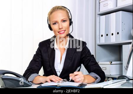 Eine freundliche junge Frau mit Headset im Kundendienstcenter telefoniert mit einem Kunden. Freundliche Hotline, Mitarbeiterin, Call Center, Sekretäre Stockfoto