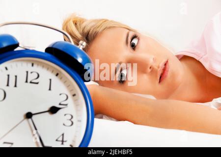 Schlaflosigkeit mit Uhr in der Nacht. Junge blonde Frau kann nicht schlafen, Wecker zeigt 2.25 Nachts, Stockfoto